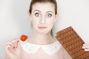 Beautiful young woman choosing to eat chocolate or a fresh strawberry.-1